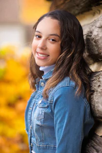 a young girl in a denim jacket leaning against a log
